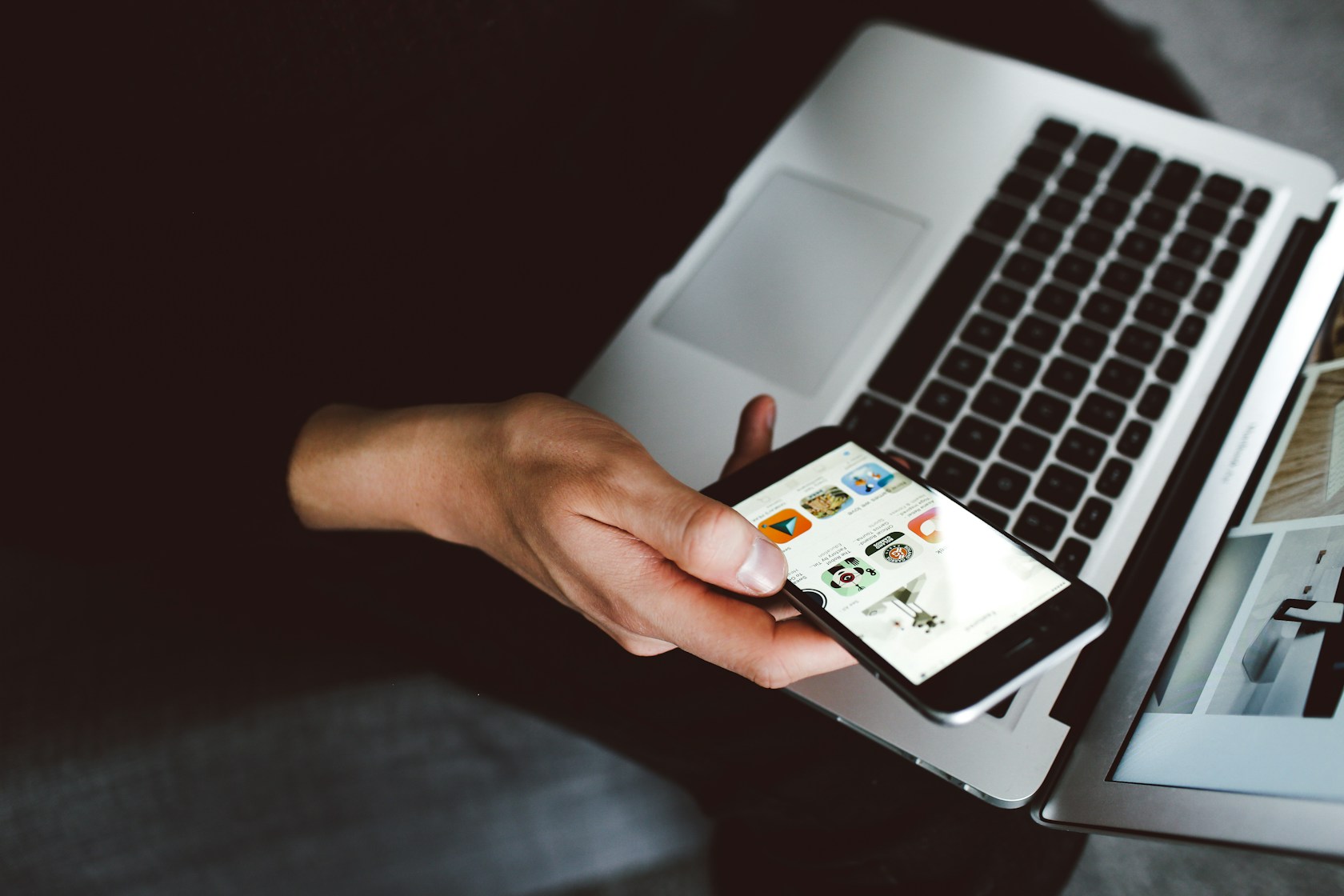 Mano sosteniendo un móvil junto a un portátil para comparar opciones por internet