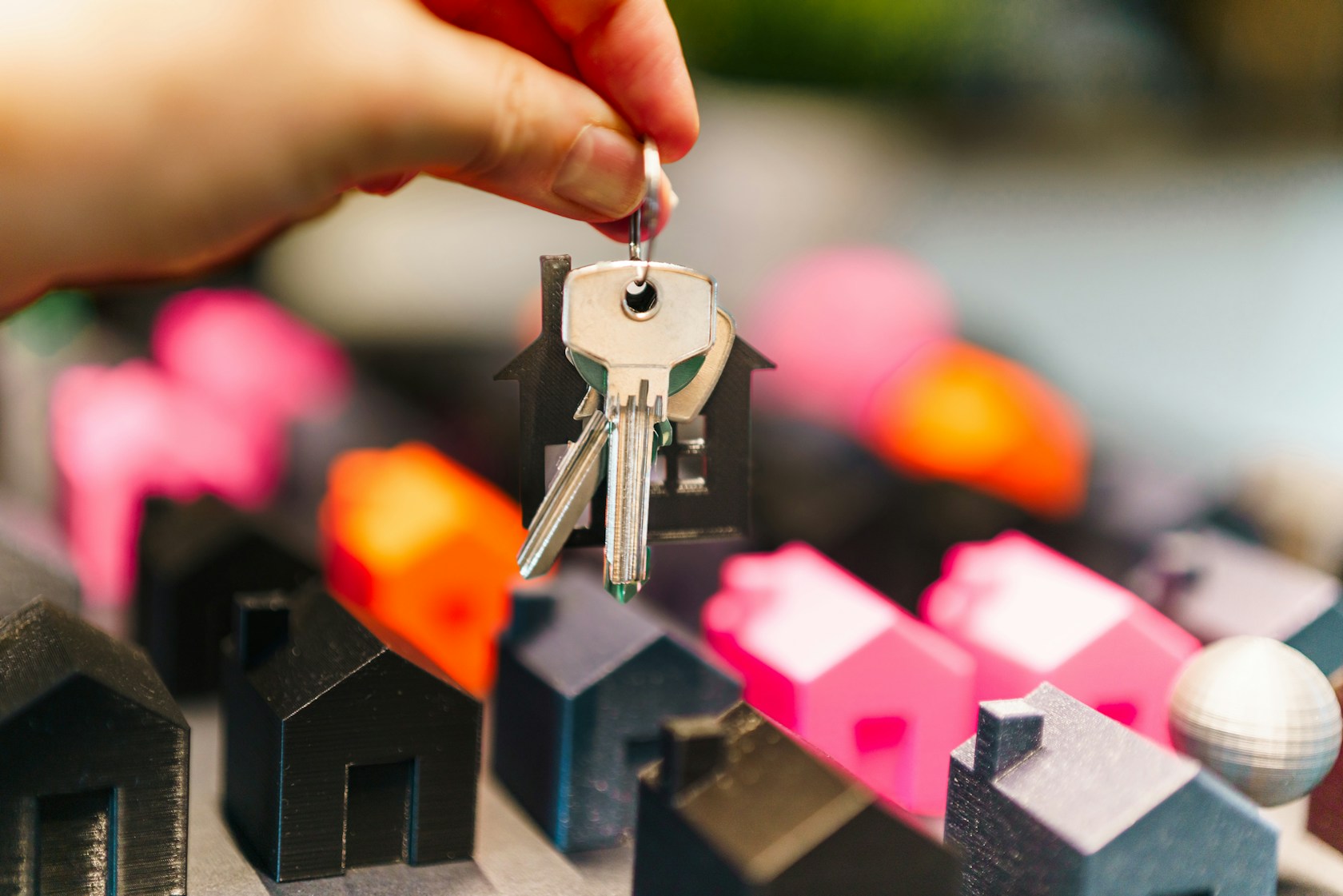 Requisitos del préstamo con garantía hipotecaria: mano con llaves de una vivienda en propiedad sobre maquetas de casas